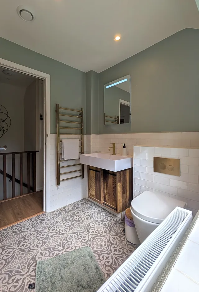 The bathroom basin on a reclaimed-wood vanity, a wall-hung WC, brass heated towel rail and patterned floor tiles