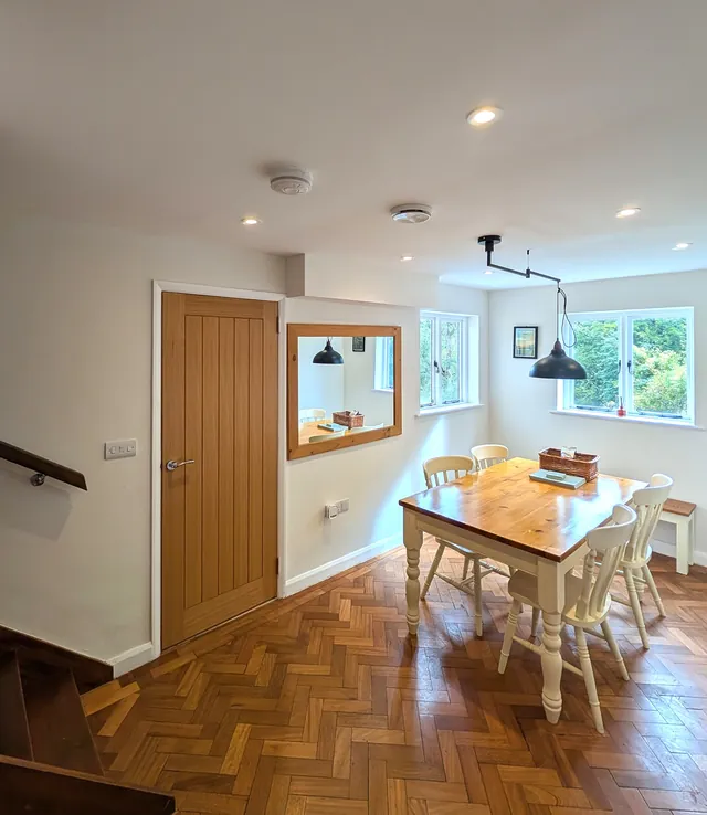 The dining area with herringbone parquet, an oak door, a mirror and a table for four by the windows
