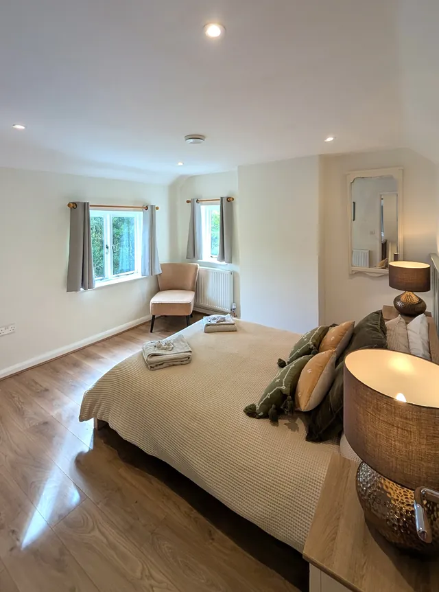 The double bedroom from the bedside, with two windows, an armchair and soft natural light
