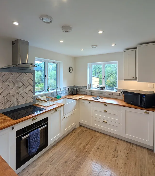 The kitchen with oven and hob, Belfast sink, microwave and two windows looking out to trees