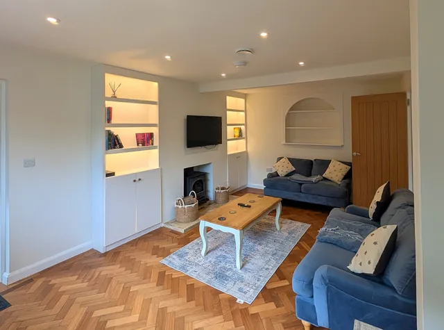 The living room seen from the doorway, with lit shelves either side of the wood burner and two blue sofas